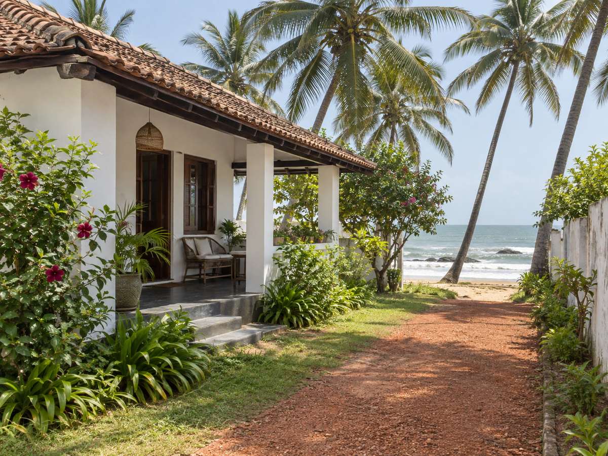 Whitewashed guest-house facade with clay tiles and a laterite garden path to the sand